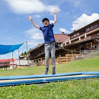 Ein fröhliches Kind springt auf einem Trampolin - im Hintergrund befindet sich das Hotel Ramsi.