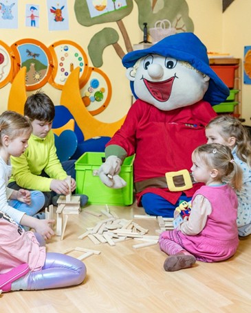 Kinder spielen gemeinsam mit Ramsi-Maskottchen im bunt gestalteten Kinderclub und bauen mit Holzbausteinen.