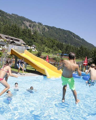 Ein Mann filmt Kinder wie sie in einen Pool mit einer gelben Rutsche springen.