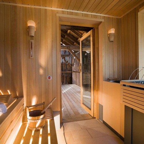 Cozy sauna with a view of the outdoors, plenty of seating, an infusion bucket and wall lights.