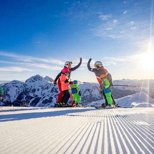 Mutter und Vater, geben sich ein High five auf einer Skipiste während ihre drei Kinder daneben stehen und zusehen.