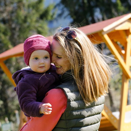 Eine lächelnde Mutter, die mit dem Rücken zur Kamera steht, hält ihr Baby im Arm.