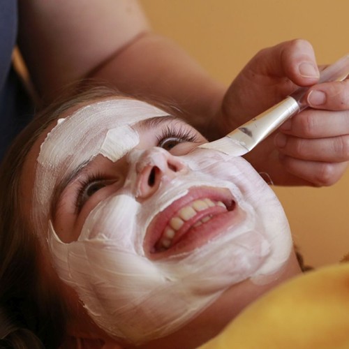 Mädchen bekommt von einer Ramsi-Mitarbeiterin eine Gesichtsmaske aufgetragen und lacht fröhlich.